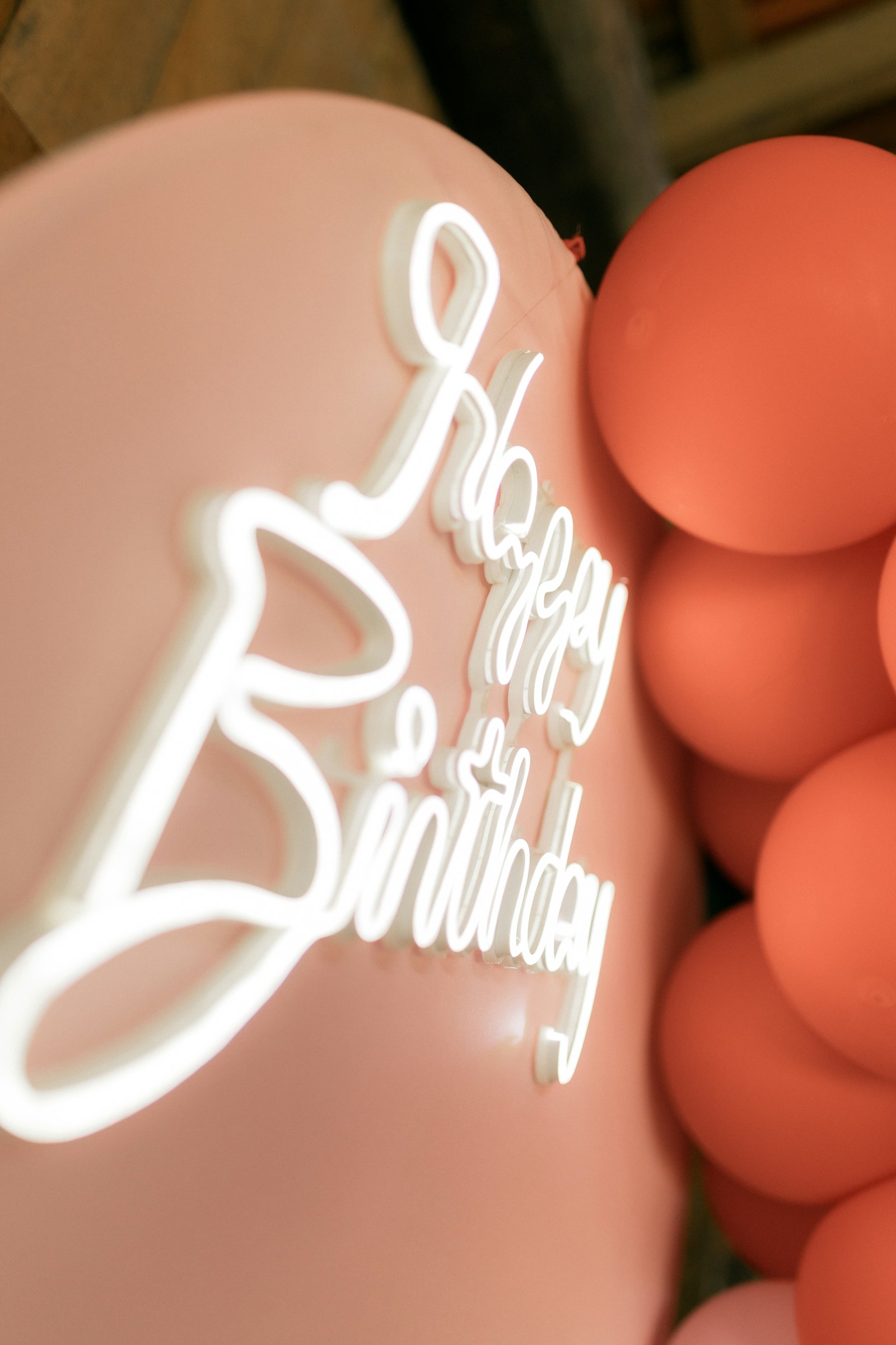 Close-up of a glowing Happy Birthday sign surrounded by pink balloons